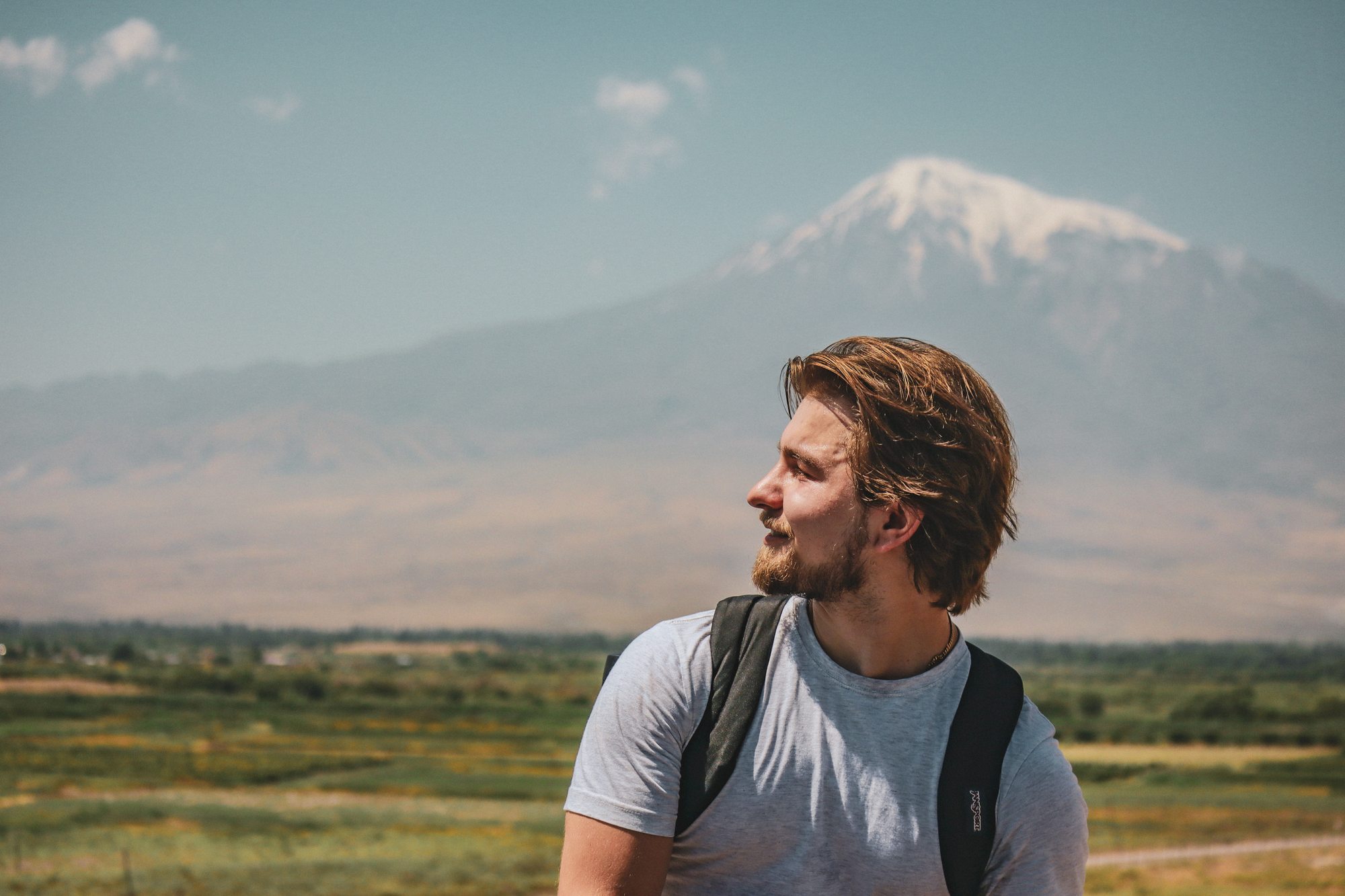 Nishan standing at Khor Virap with Mount Ararat — the snow-capped symbol of Armenian identity — rising behind him across the valley on a clear blue day