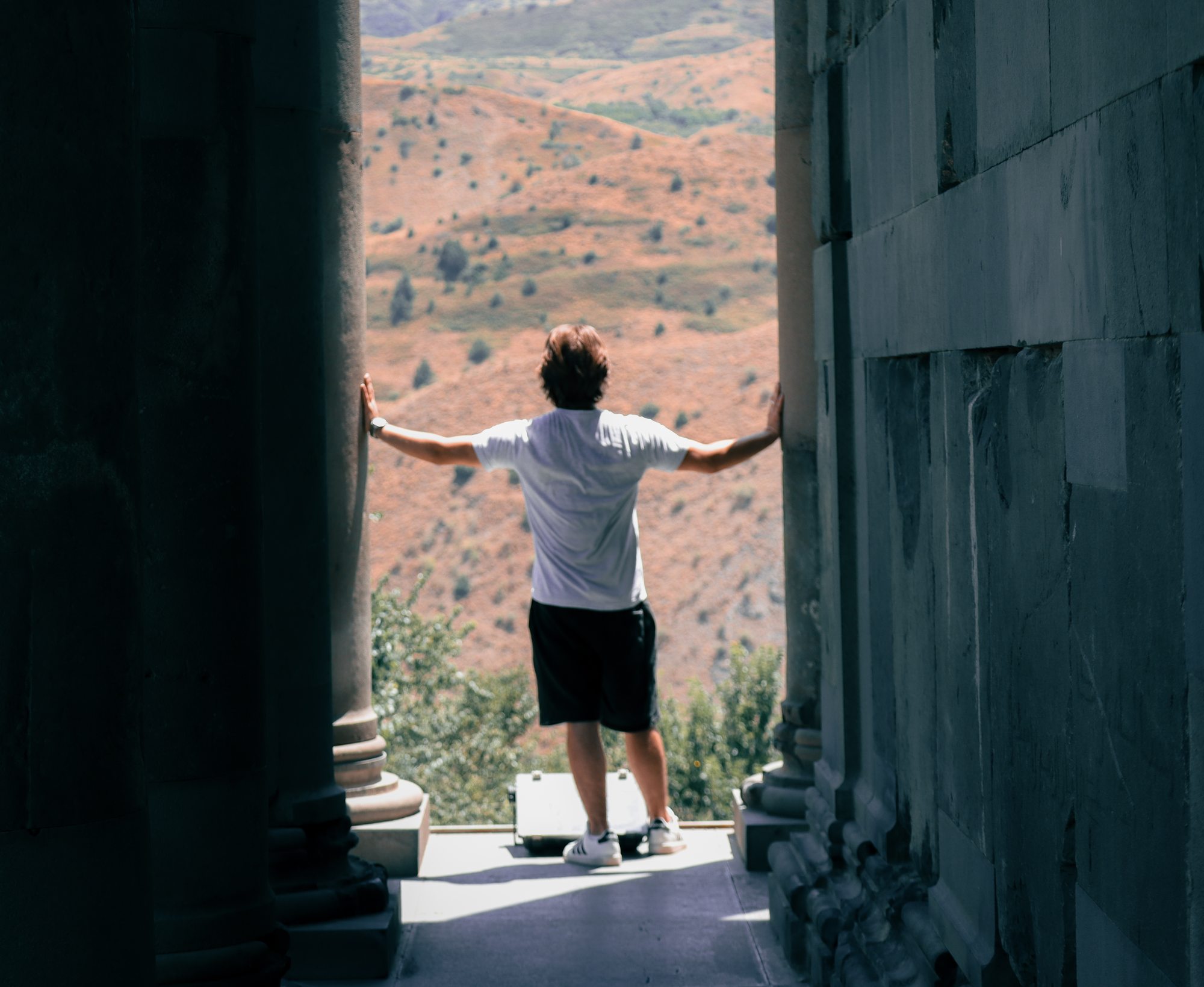 Nishan standing in the doorway of an ancient Armenian structure, arms spread, looking out at the vast landscape of the Armenian countryside