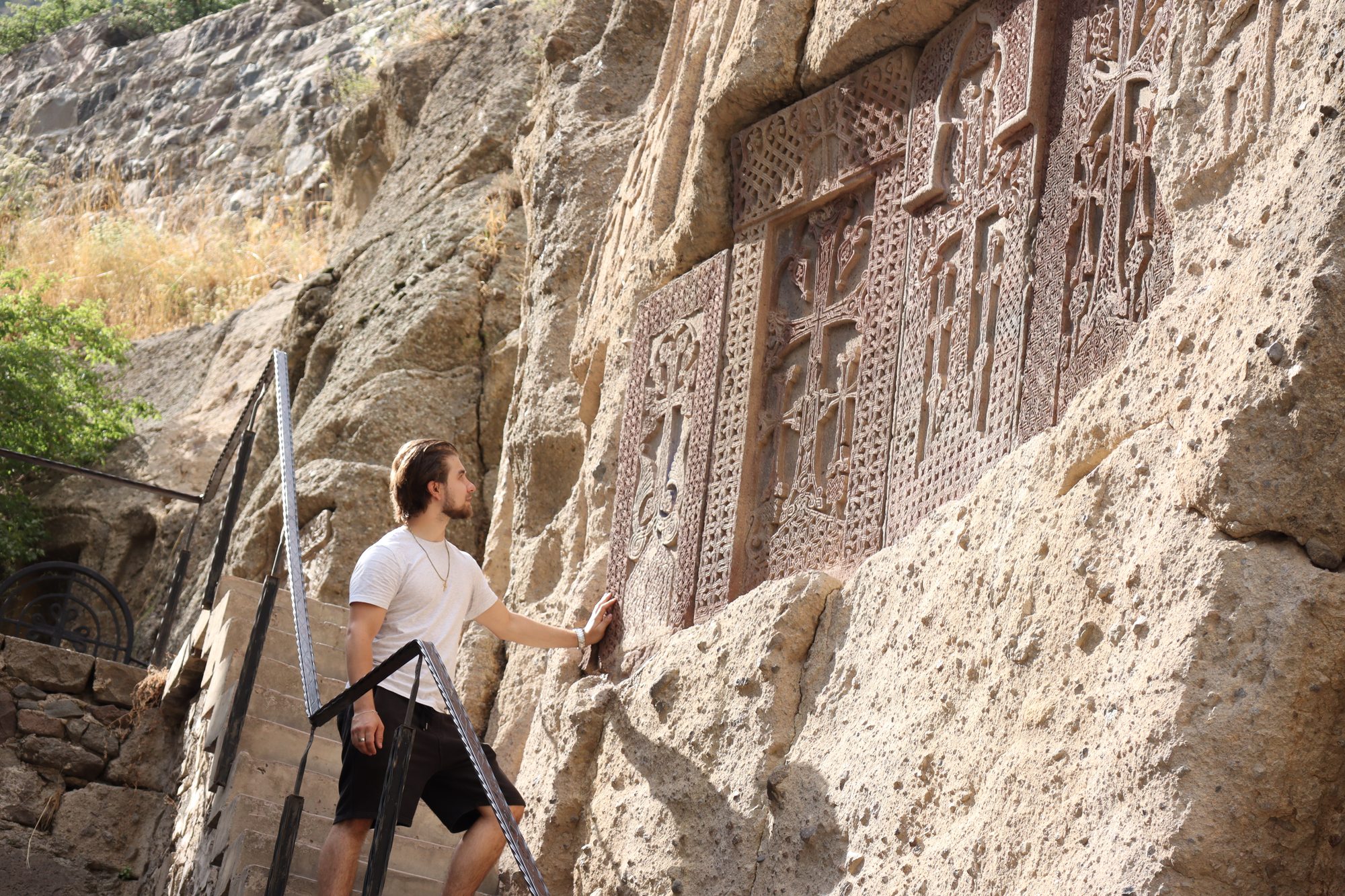 Nishan reaching out to touch khachkars — Armenian cross-stones — carved directly into the rock face at Geghard Monastery