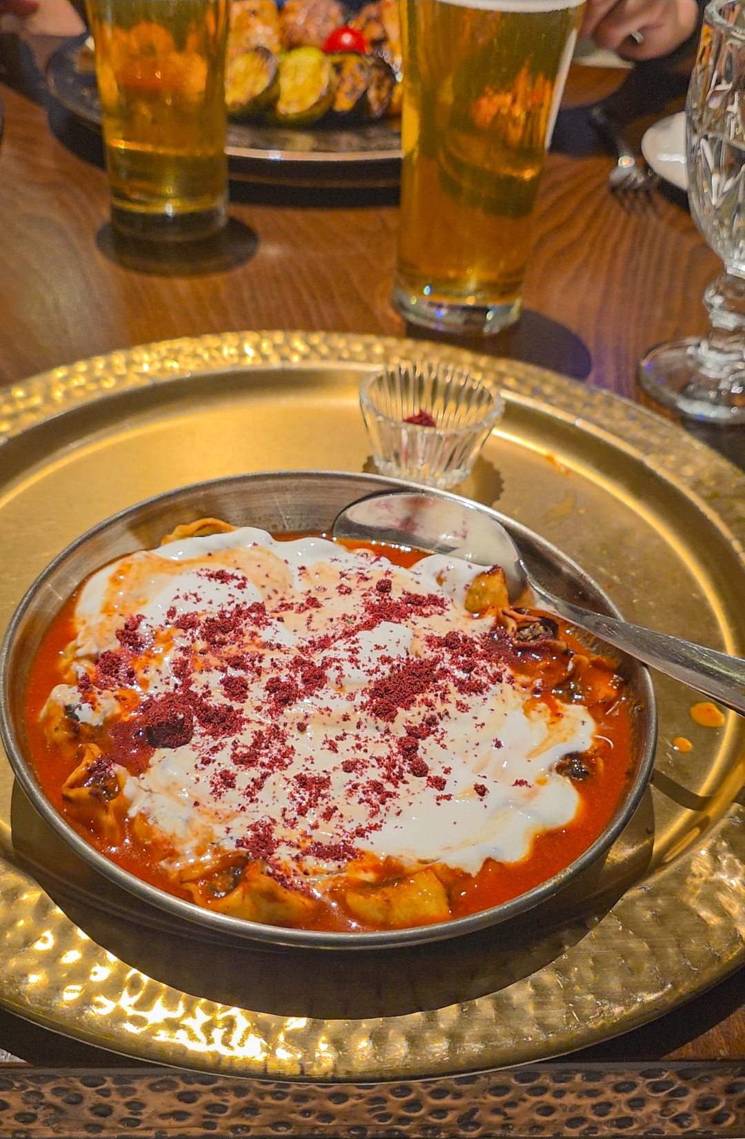 A bowl of Armenian manti at Mayrig restaurant in Yerevan — small baked dumplings in a rich tomato sauce, topped with thick white yogurt and dusted with deep red sumac, served on a hammered gold tray