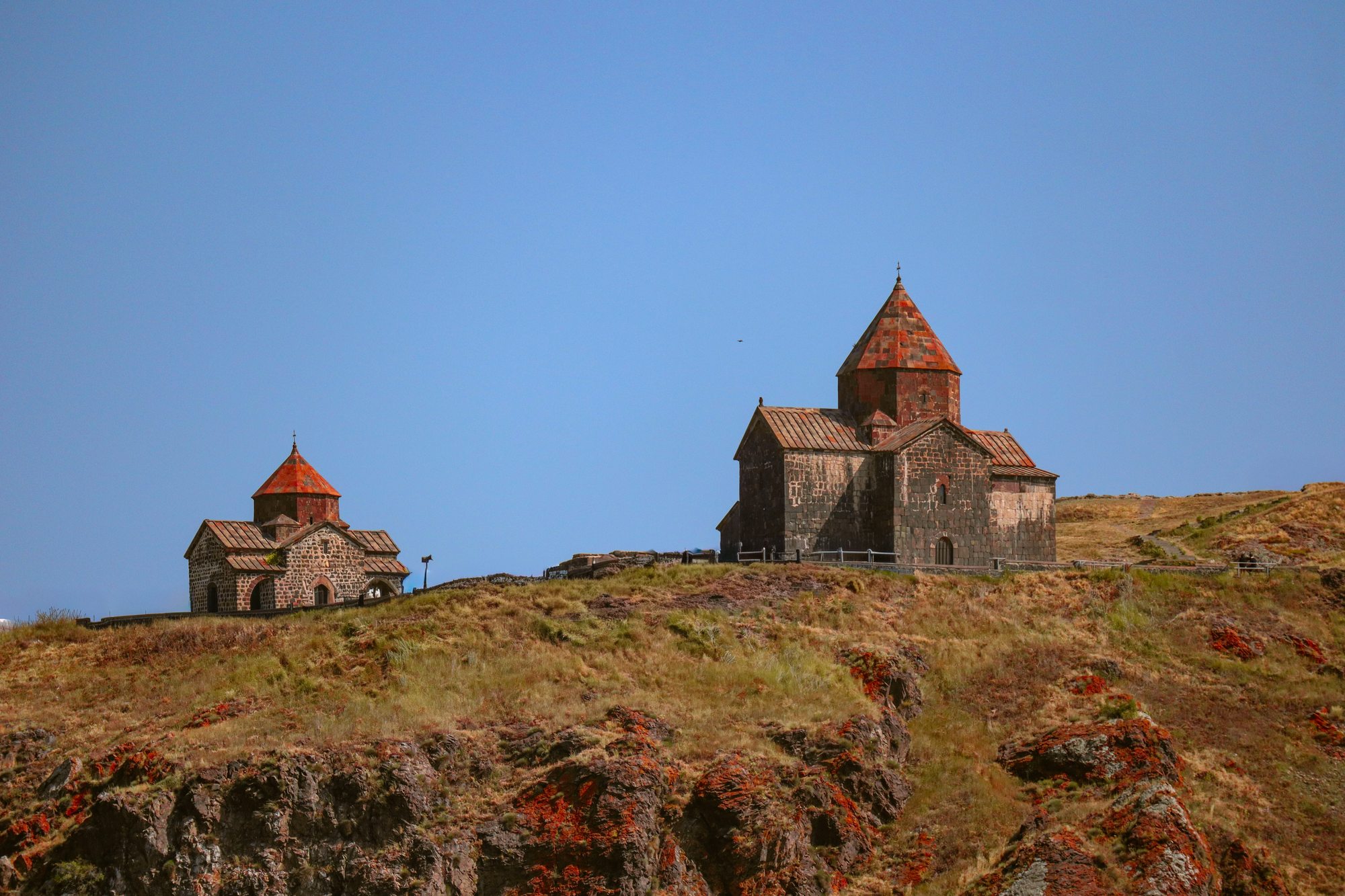 Sevanavank monastery complex perched on the rocky peninsula above Lake Sevan — two ancient stone churches against a perfect blue sky