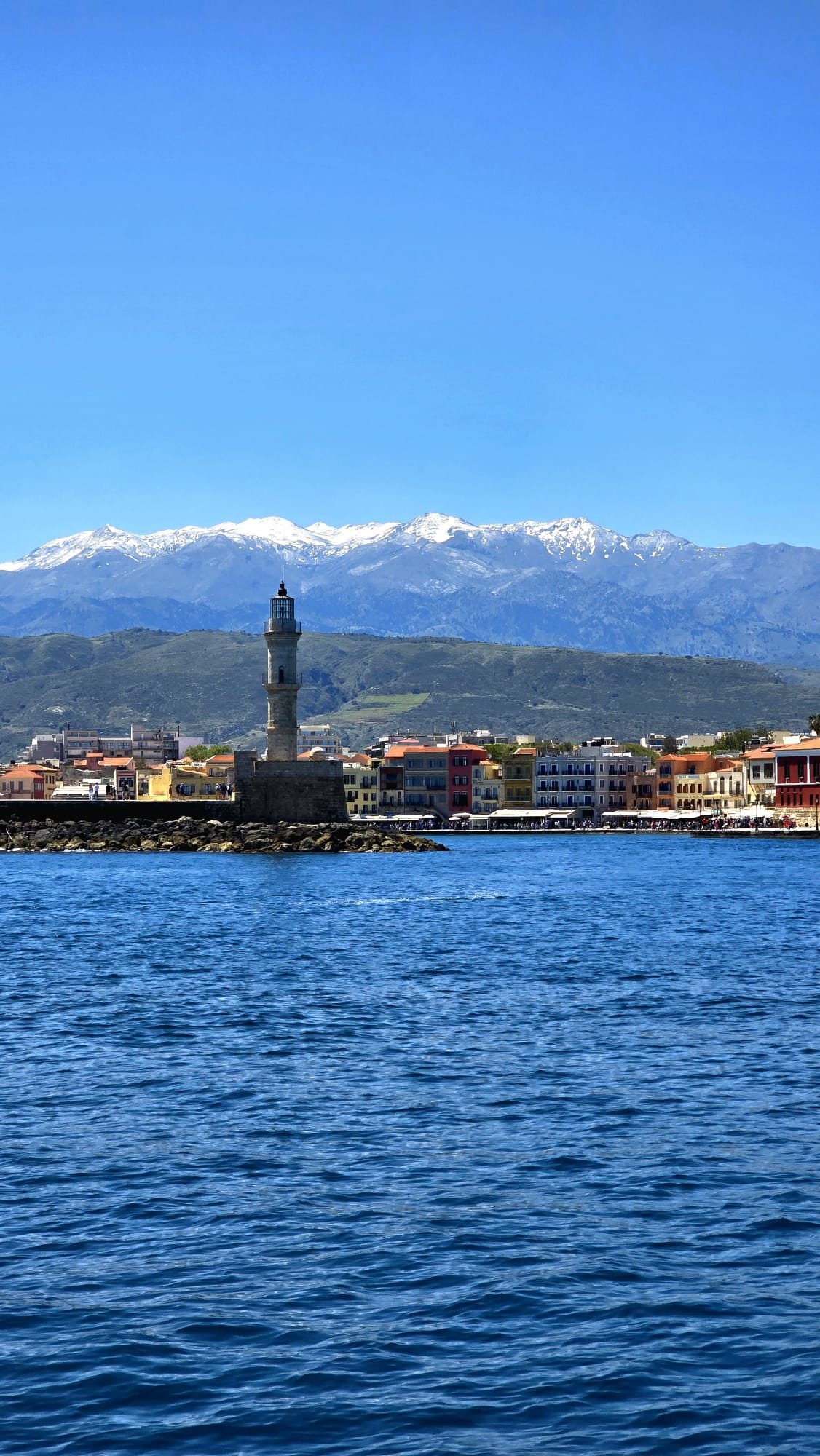 The Crete waterfront — a Venetian-era lighthouse and harbour buildings seen across the calm water of the old port