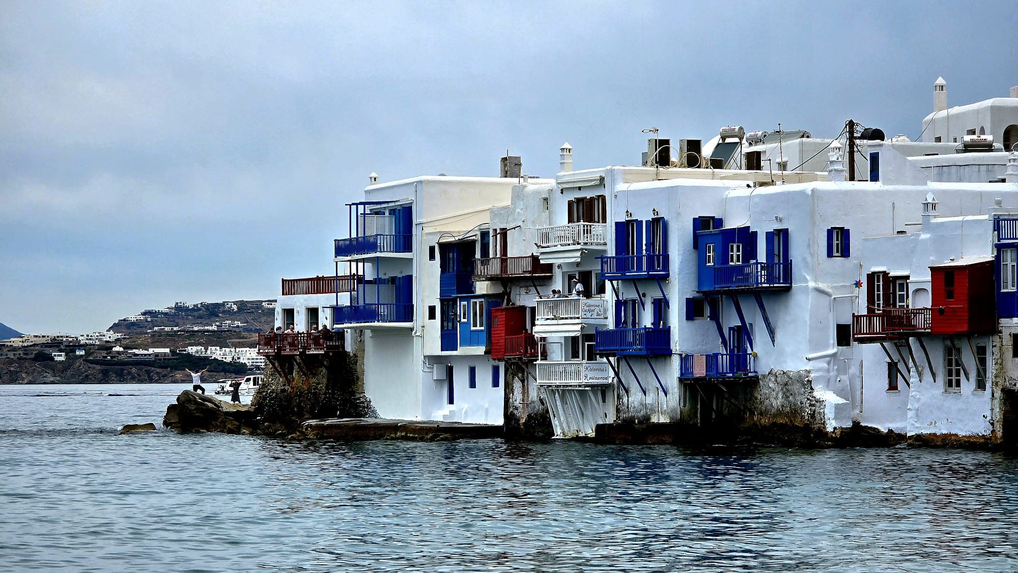 The harbour at Mykonos — fishing boats and waterfront tavernas along the edge of the bright blue Aegean