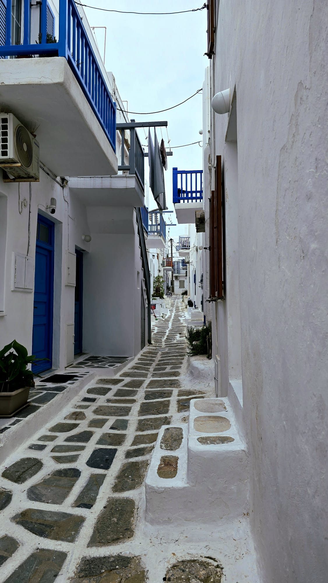 A narrow Mykonos street — whitewashed walls, blue shutters and bright pink bougainvillea spilling over a doorway