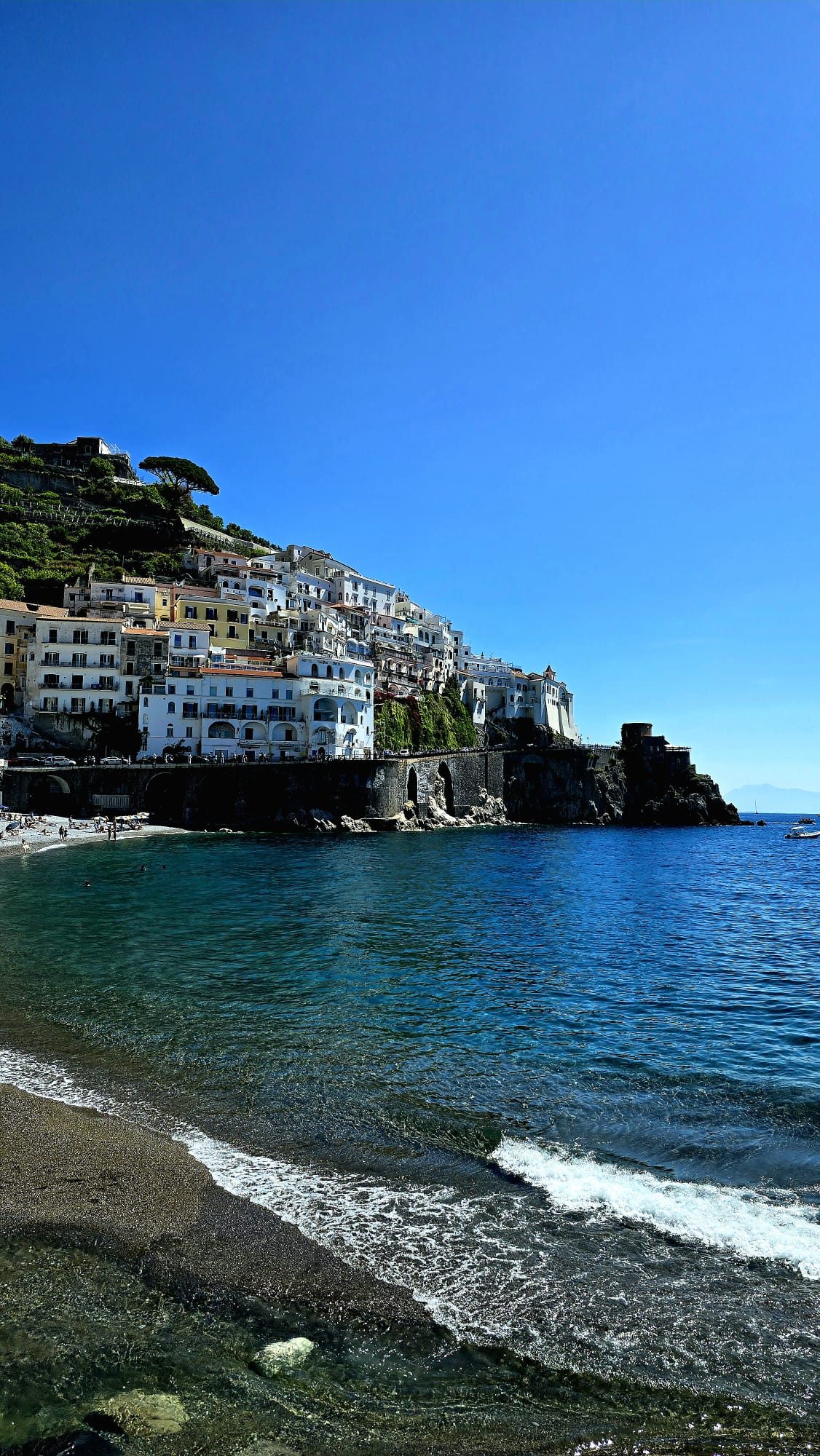 The town of Amalfi seen from the water — whitewashed buildings and a cathedral tucked into a steep green cliff above the harbour