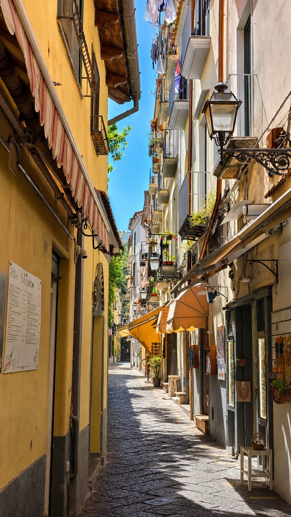 A narrow Sorrento alley lined with shopfronts and shuttered pastel buildings, washing strung between the walls above