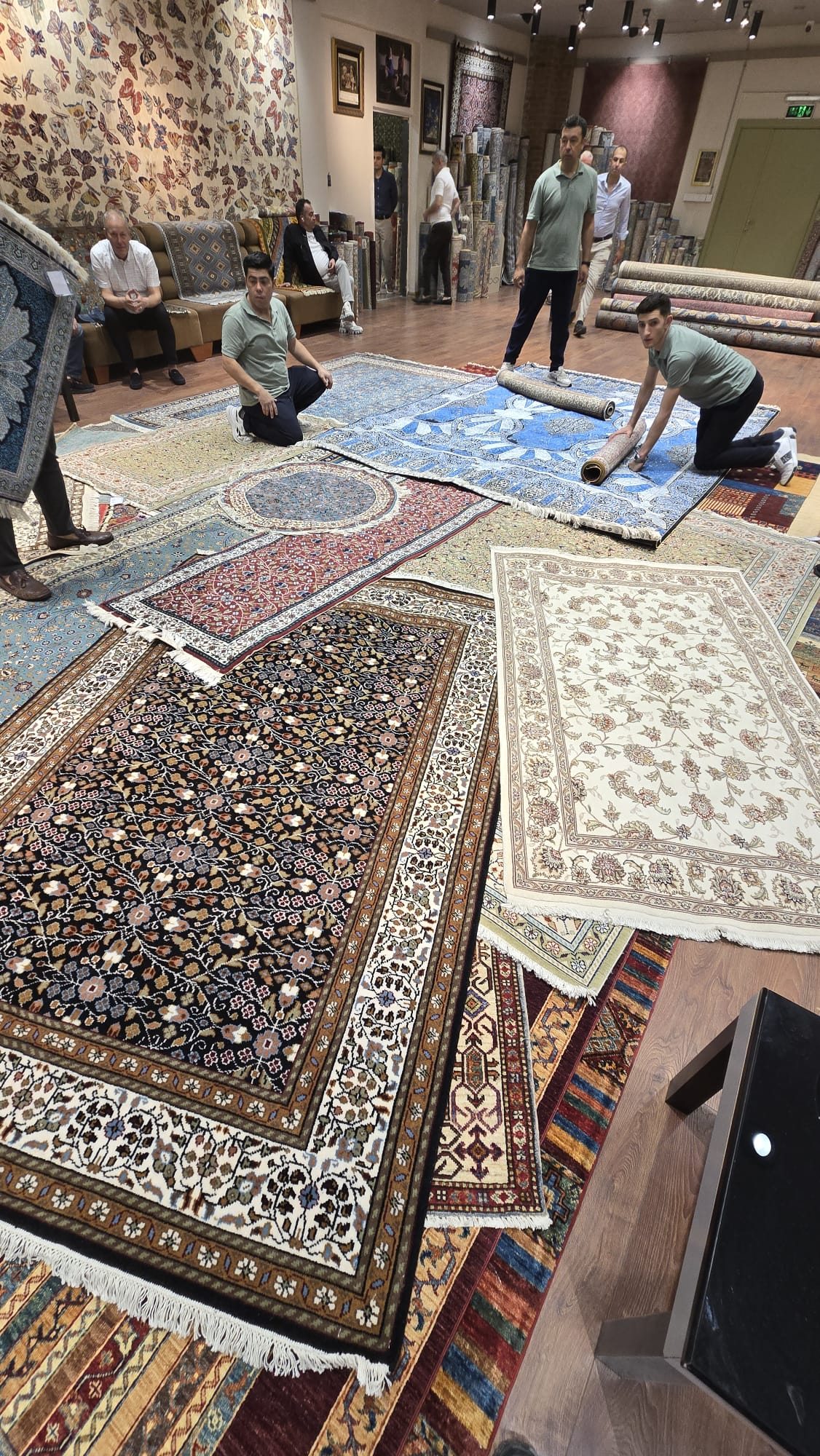 A carpet maker near Kusadași demonstrating traditional hand-weaving, rows of colourful woven rugs displayed behind