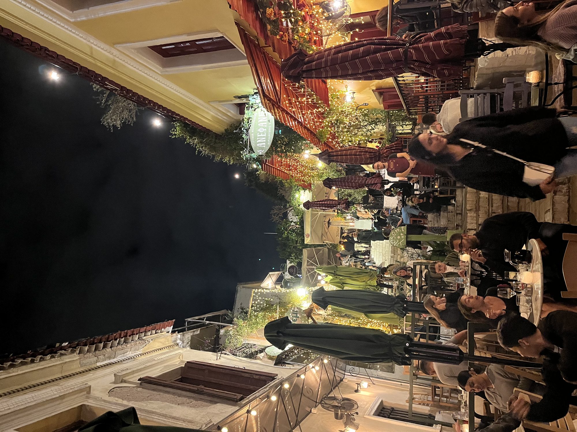 Athens nightlife — outdoor restaurants packed with people in the Monastiraki neighbourhood at night, string lights above