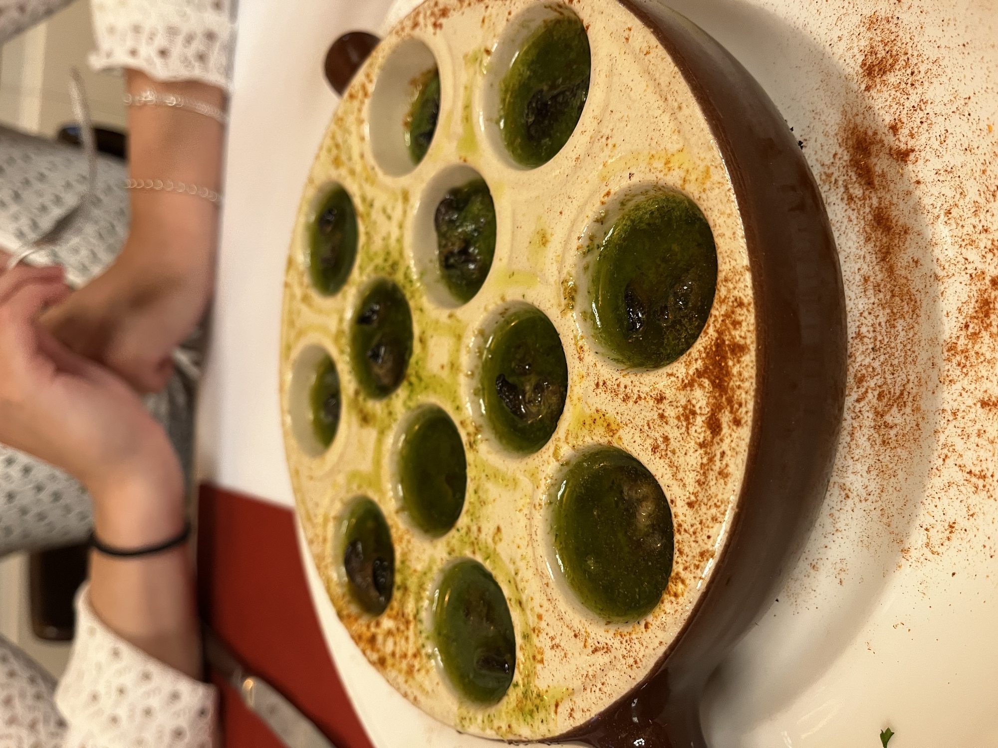 A plate of escargots de Bourgogne in their shells — green parsley garlic butter and a dusting of paprika at a Lyon restaurant
