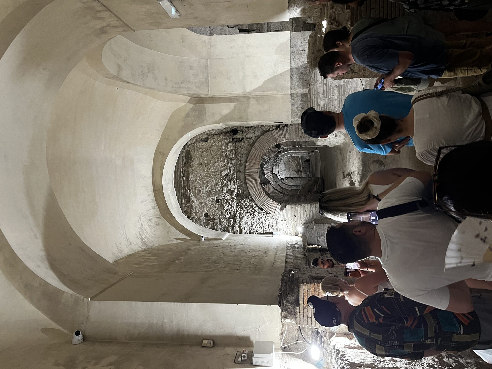 A vaulted underground cistern in the Naples Underground — visitors gathered around stone steps cut into the rock