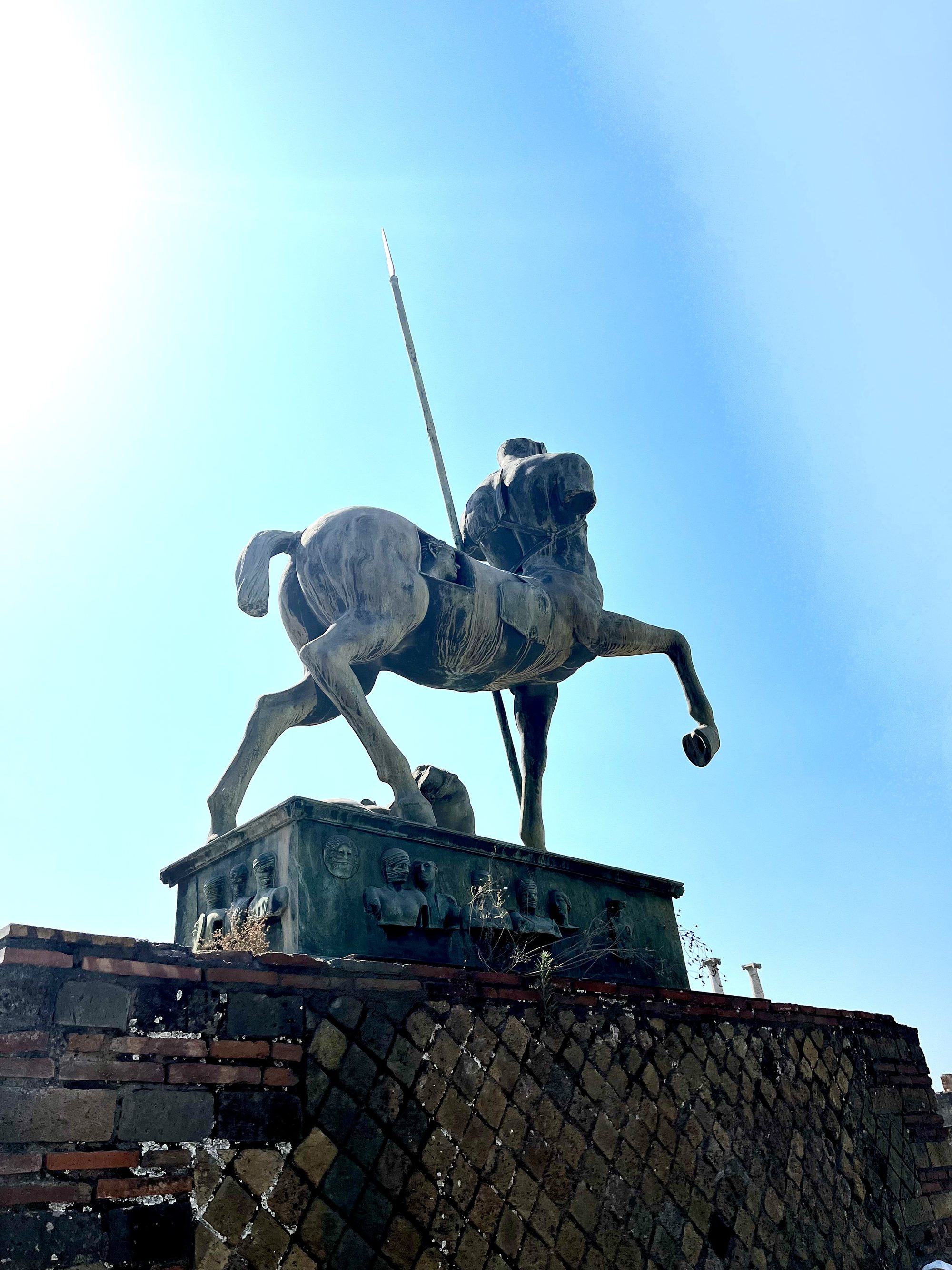The Centaur statue at Pompeii seen from below against a brilliant blue sky — spear raised, the ancient Forum stretching out below