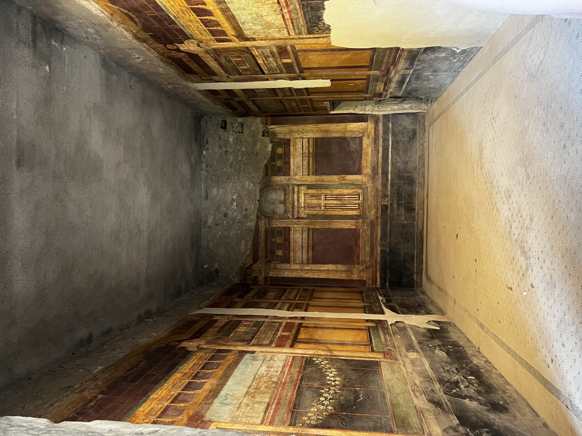 A preserved painted room in Pompeii — ornate yellow, red and black frescoes covering the walls of an ancient Roman chamber