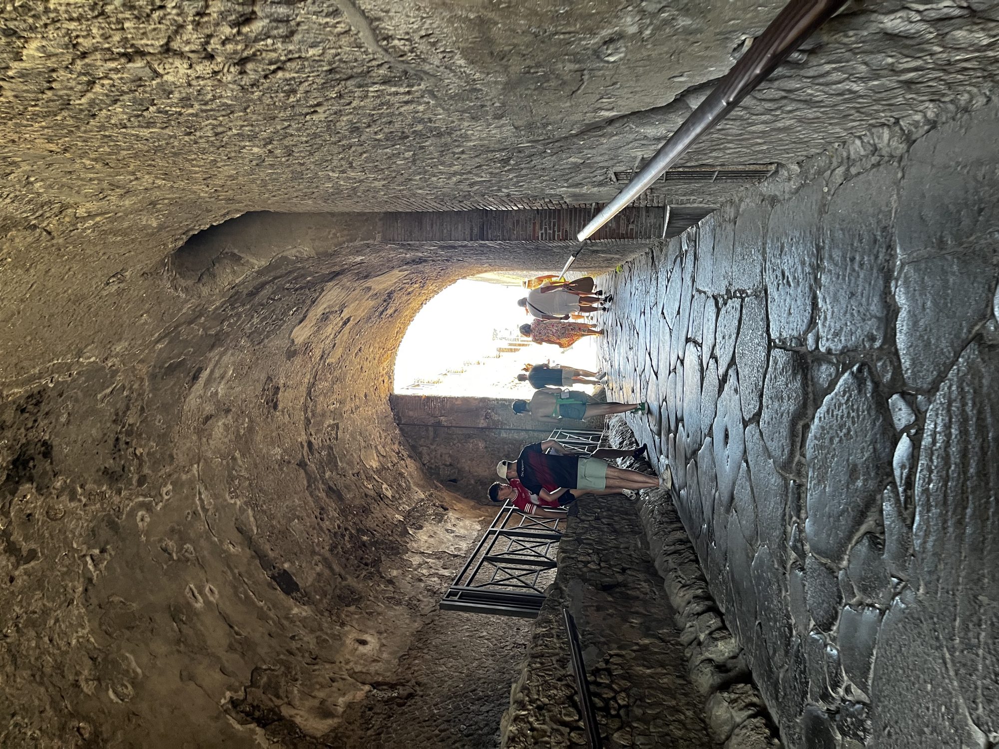 The ancient stone tunnel entrance to Pompeii — cobblestone road worn smooth over two thousand years, visitors passing through
