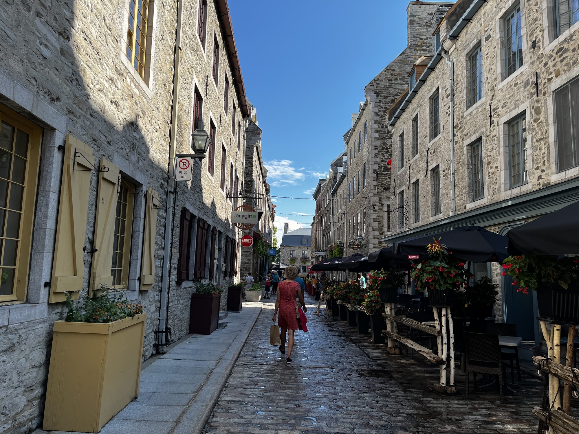 A narrow cobblestone street in Petit Champlain, Old Quebec, with stone buildings on either side and a woman in a red dress walking down the middle