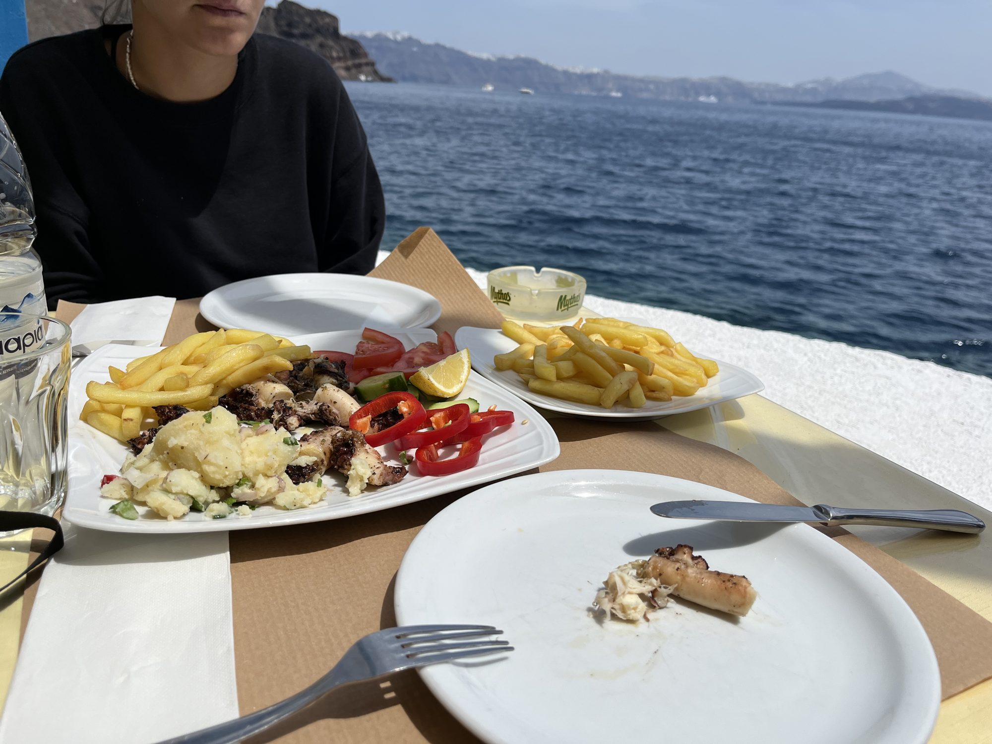 Grilled octopus and Greek sides at a waterfront restaurant in Santorini, Aegean Sea in the background