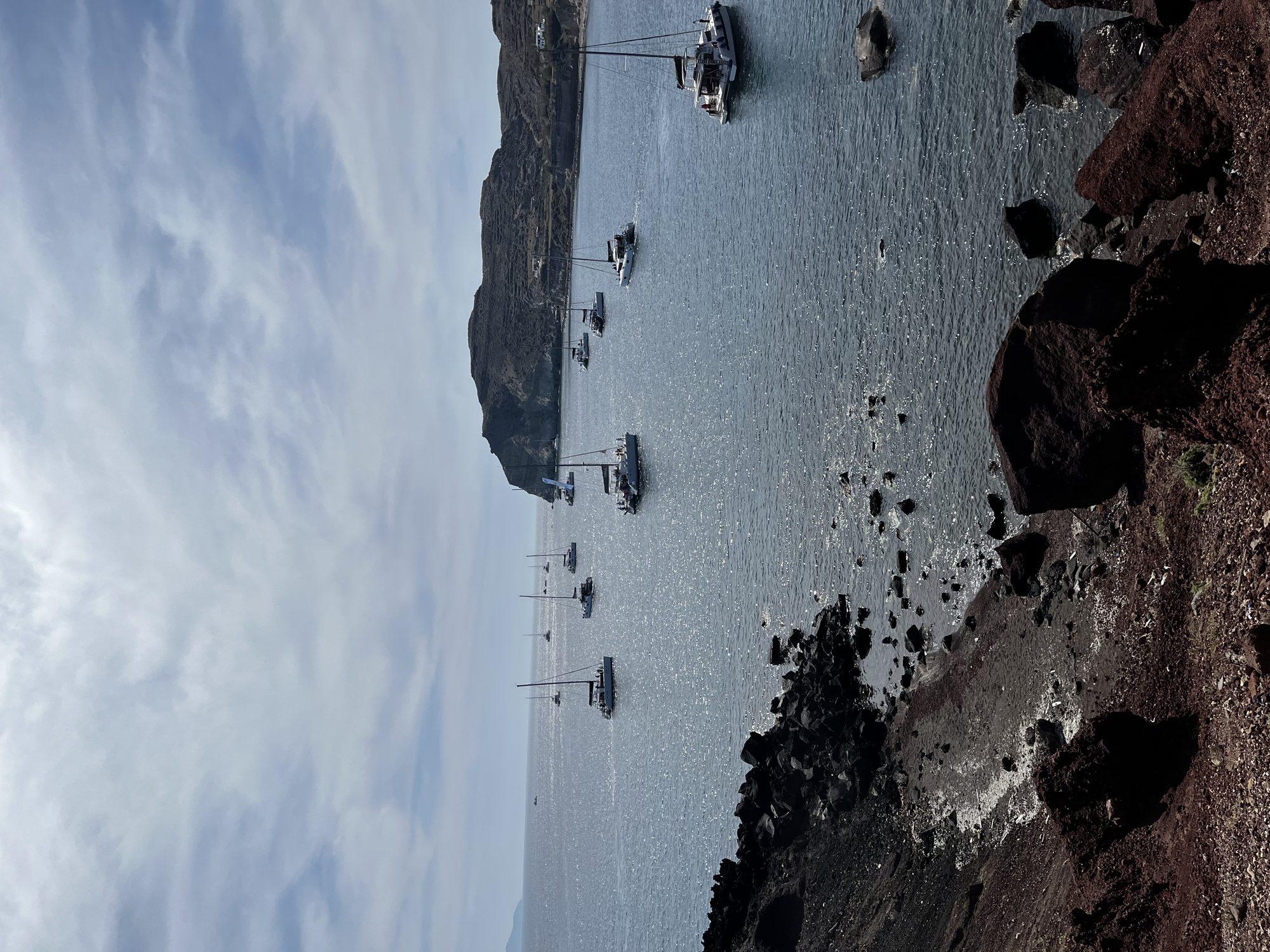 The Red Beach of Santorini — volcanic red cliffs descending to turquoise water, hikers on the path above