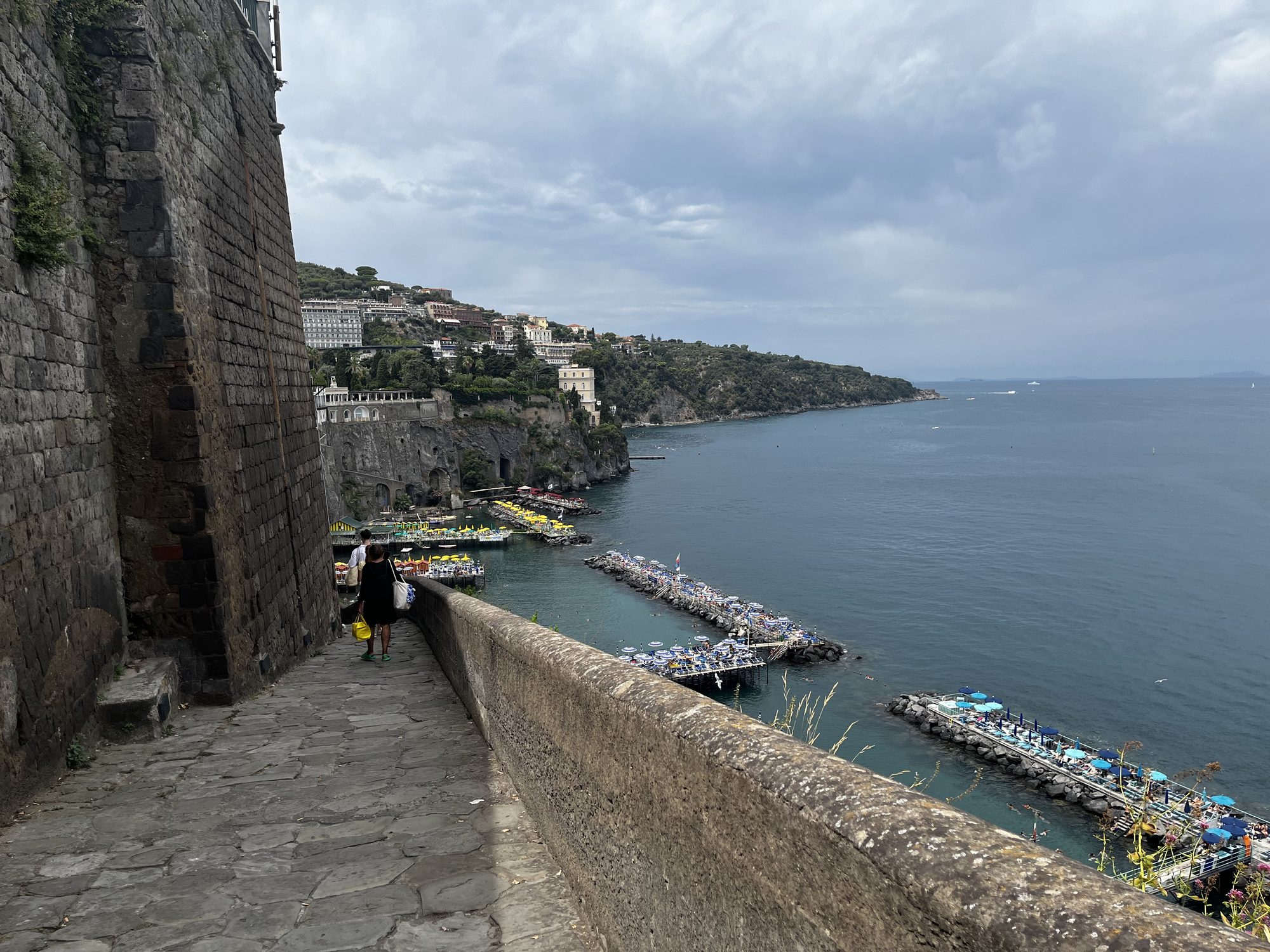 The ancient cliff walkway in Sorrento — stone walls above the beach clubs and the Bay of Naples stretching out below