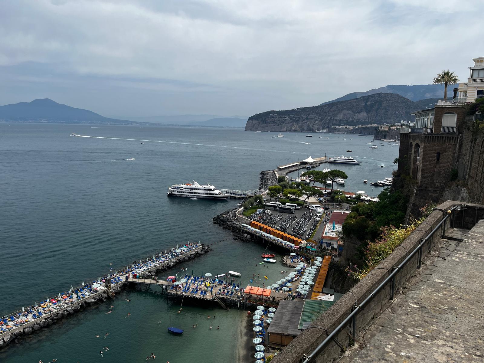 Sorrento harbour from above — the port, beach clubs, and the Bay of Naples stretching toward Vesuvius