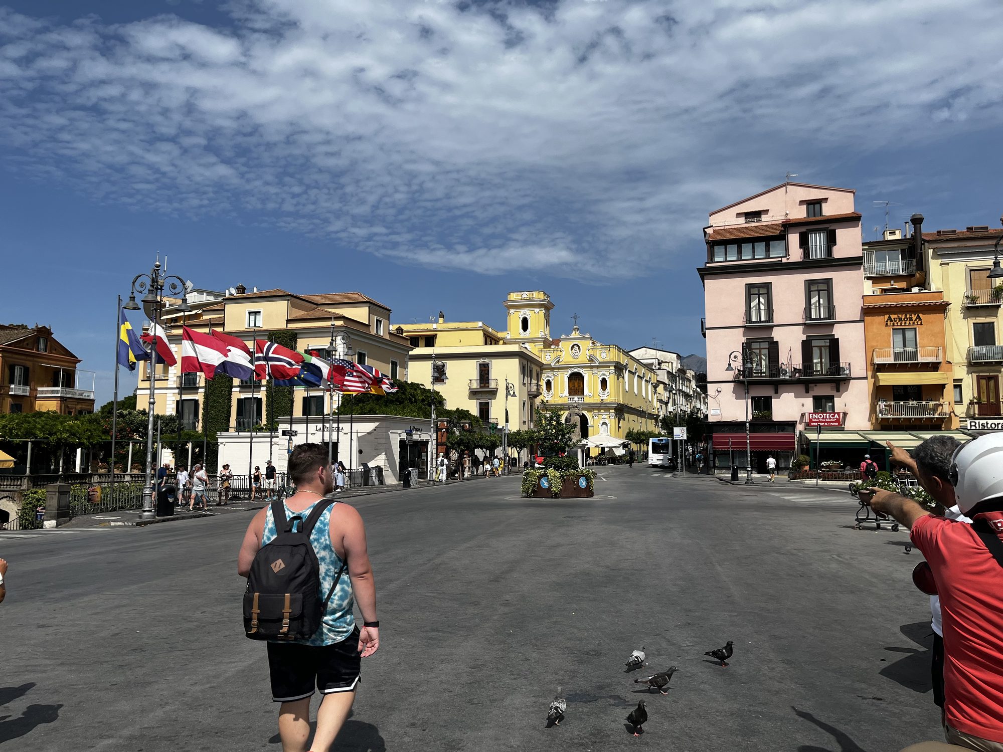 Piazza Tasso in Sorrento — the main square with international flags, motorcycles, and the yellow baroque church facade